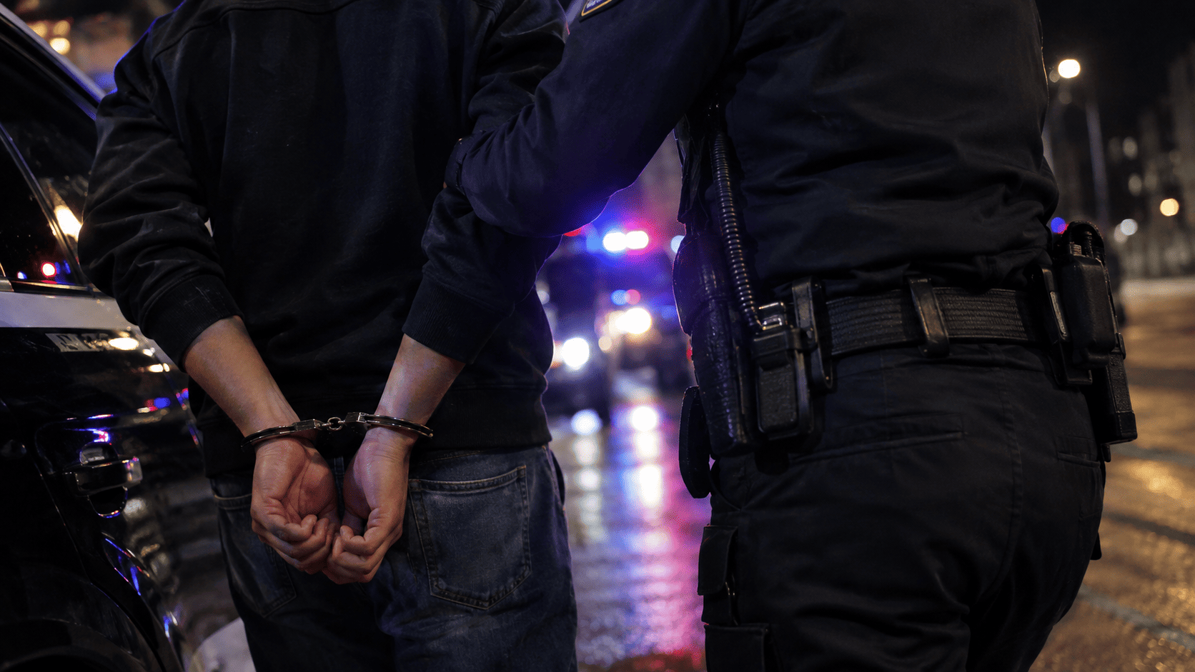 Person in handcuffs standing beside an officer at night after an arrest for assault on a police officer in Franklin County.